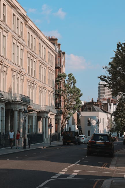 A street scene featuring a row of white Victorian-style terrace houses with ornate architectural details, large windows, and decorative railings on the balconies. The buildings are three to four stori